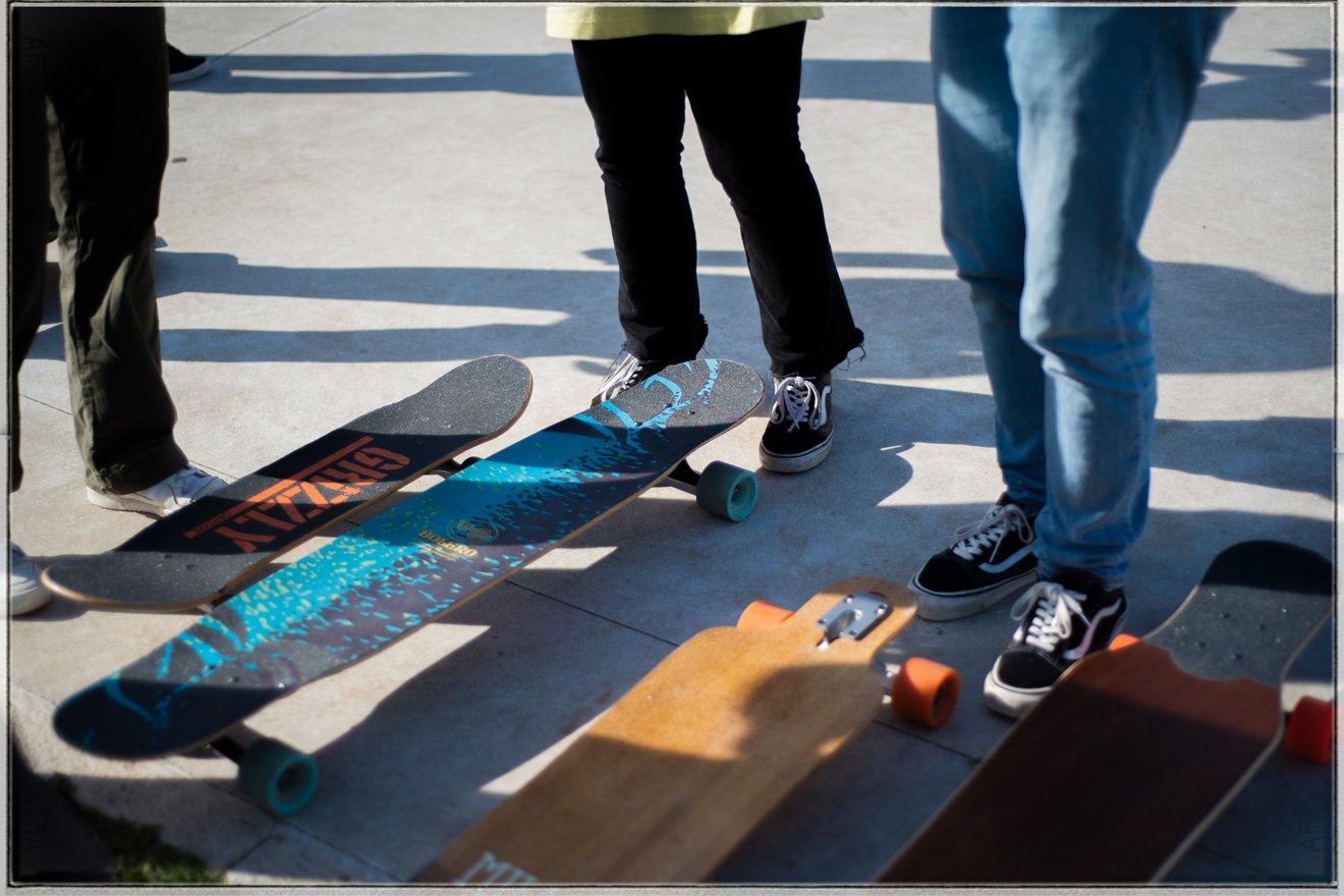 Group of skateboarders standing on concrete with skateboards on the ground in sunlight.