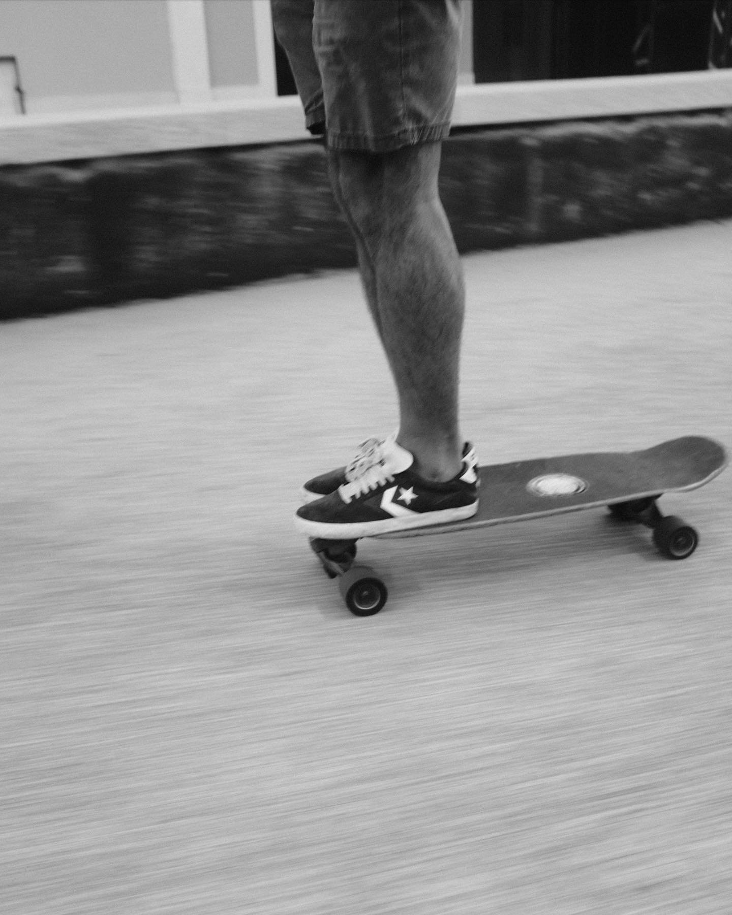 Close-up of a person skateboarding indoors, wearing shorts and sneakers, with focus on their legs and skateboard in motion, black and white photo.