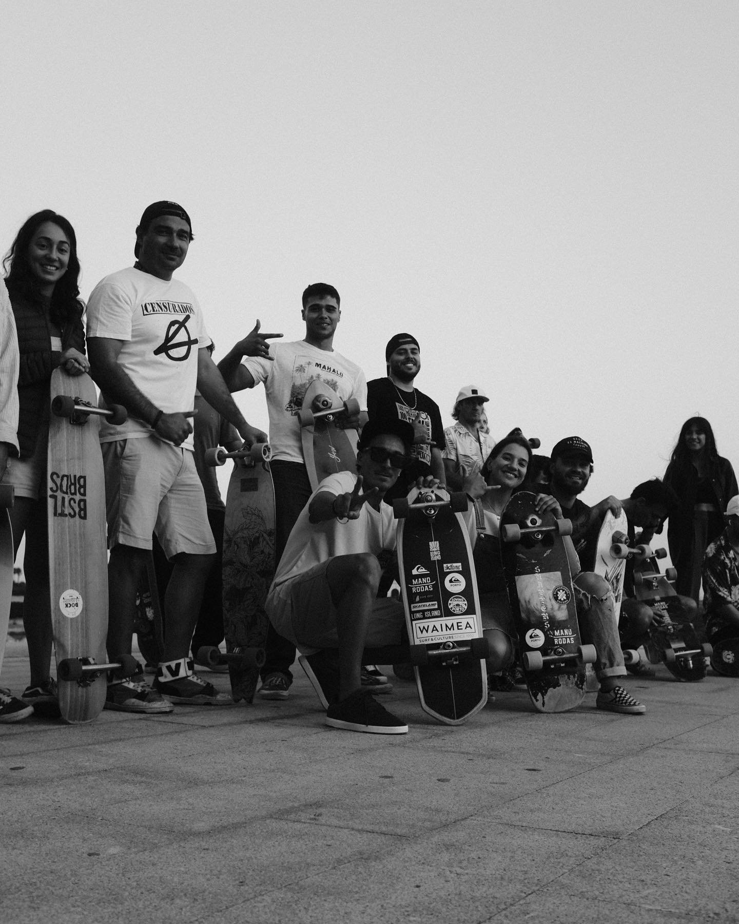 Group of people posing with skateboards outdoors, some standing and some kneeling, in a black-and-white photo.