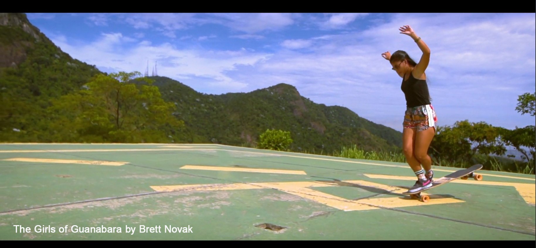 A girl skateboarding on a green surface with mountain scenery in the background.