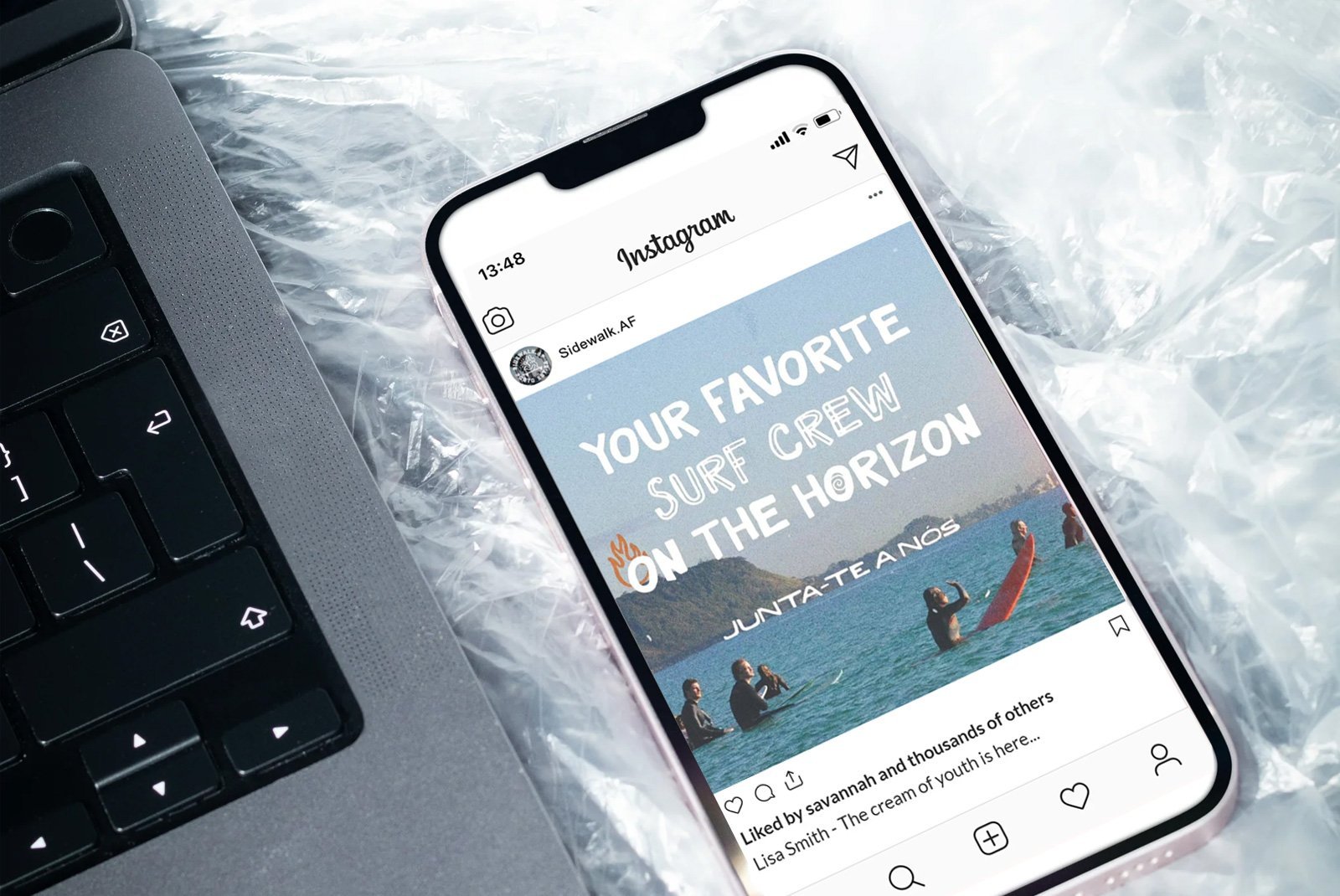 A smartphone displaying an Instagram post about a surf crew at the beach, placed next to a laptop on a plastic surface.