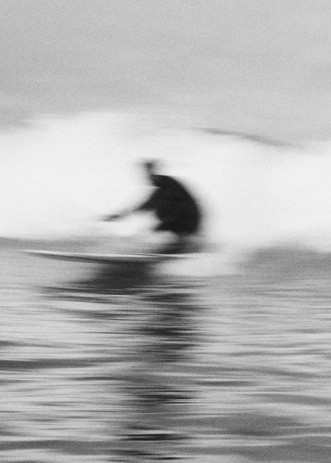A black and white photo of a person surfing on a wave, with motion blur indicating movement.