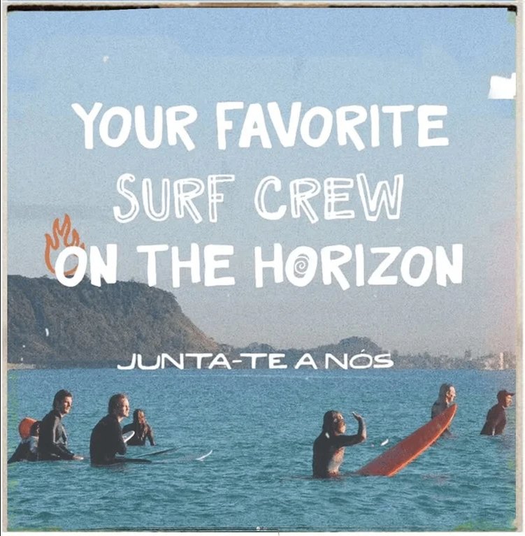 Group of surfers in the ocean, with a mountain in the background, on a sunny day.