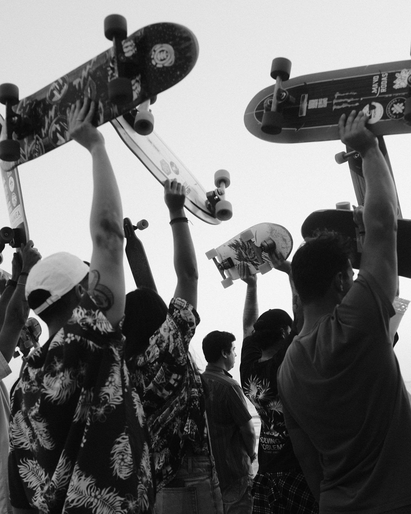Group of people raising skateboards in the air, seen from a low angle, in black and white.