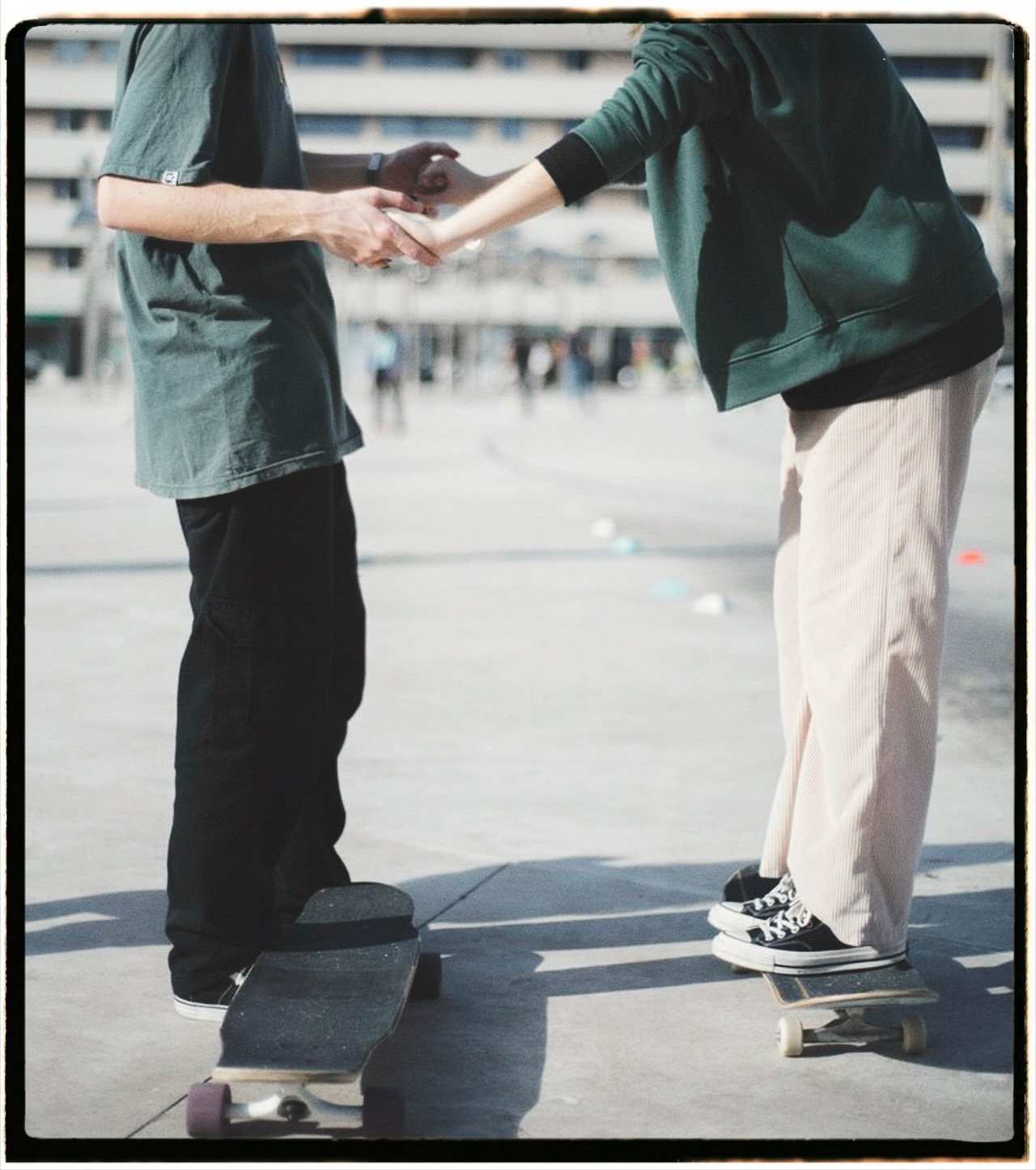 Two people standing on skateboards, shaking hands outdoors with a city background.
